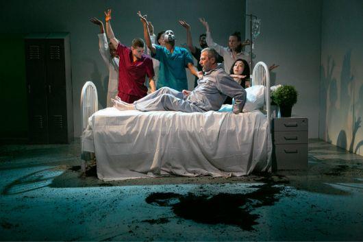 Man on hospital bed sits lays in front of healthcare workers with hands raised to the sky